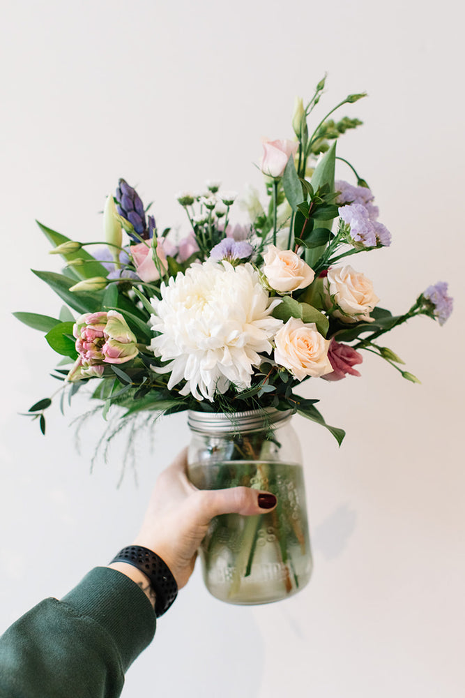 Hand holding a mason jar full of beautiful locally-grown flowers